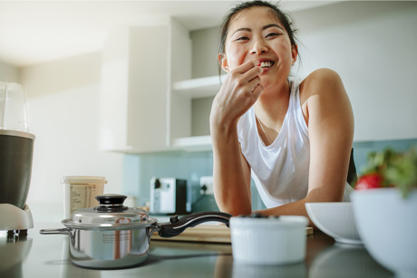 Healthy woman with Saladmaster pot, leaning on kitchen benchtop, ready for a non-toxic cookware demonstration.