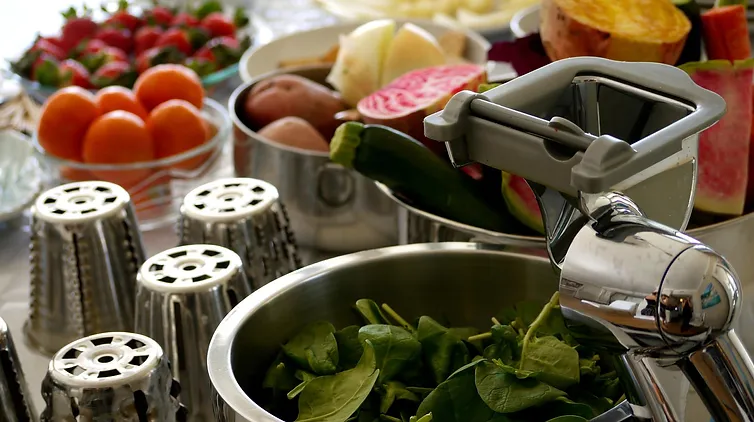 Saladmaster food processor and salad bowl surrounded by fresh fruits and vegetables for healthy cooking demonstrations.